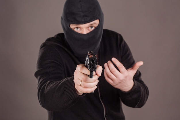 Грабитель или грабитель целится из пистолета в черную маску