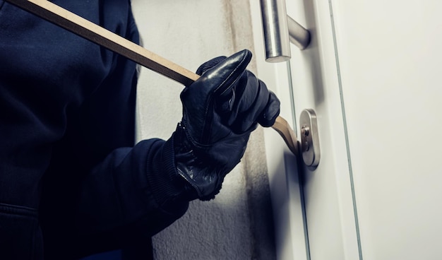 Photo burglar using crowbar to break a home door at night