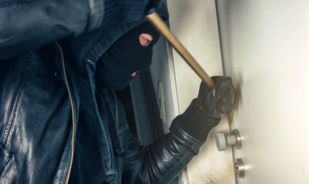 Photo burglar with crowbar breaking and entering a house door at night