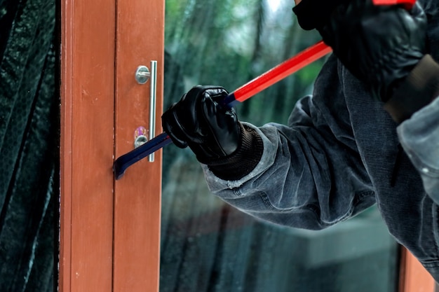 Burglar with crowbar trying break the door to enter the house