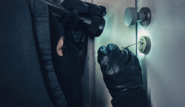 Burglar with lock picking tools and flashlight breaking into a house door