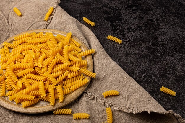 Burlap napkin on a dark structural background top view On it is a scattering of pasta in a ceramic plate Copyspace