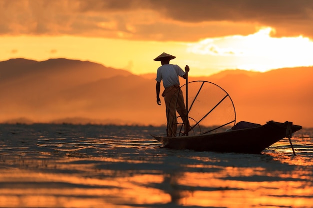 Burmese fisherman on bamboo boat catching fish in traditional way with handmade net