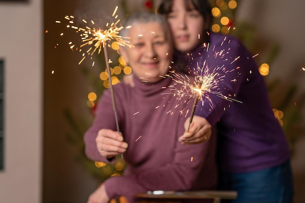 Burning bengal lights in the hands of woman and girl against the background of a Christmas tree