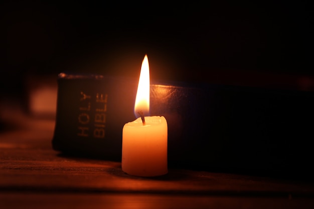 Burning candle and Bible on wooden table