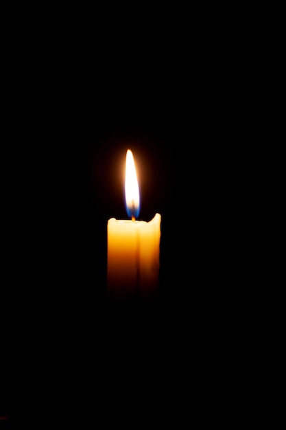 A burning candle on a black background in a dark room