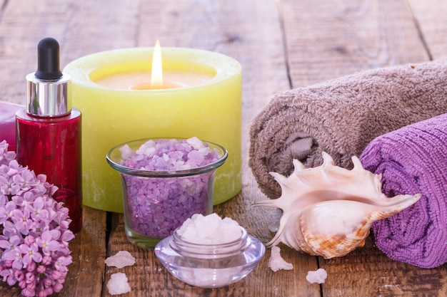 Burning candle bowls with sea salt red bottle with aromatic oil lilac flowers seashell and towels