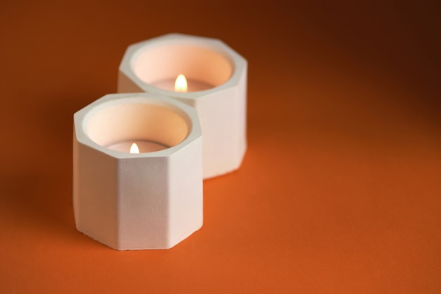 Burning candle in a concrete candle holder on orange background. Close up