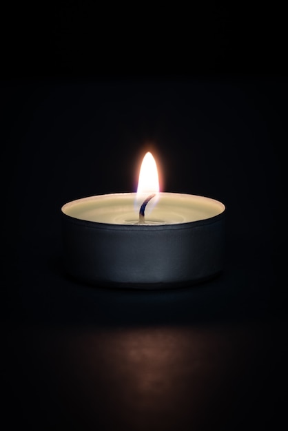 A burning candle on a dark background with a flare in the foreground