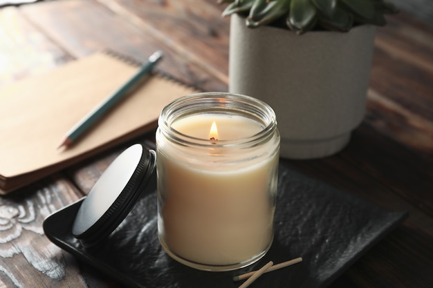 Photo burning candle in glass jar, succulent and notebook on wooden