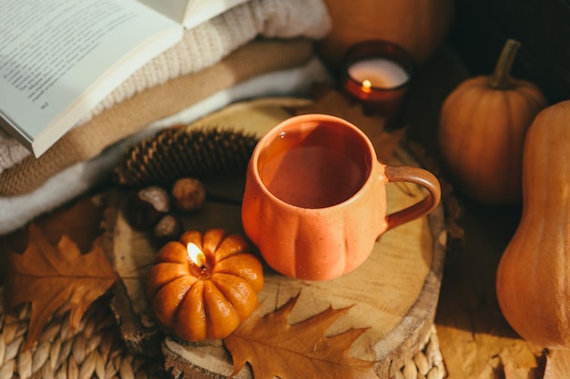 Burning candle pumpkin and a cup of tea on the background of a stack of sweaters autumn composition