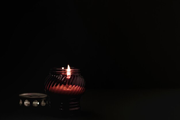 Photo burning candle in red glass candlestick on black