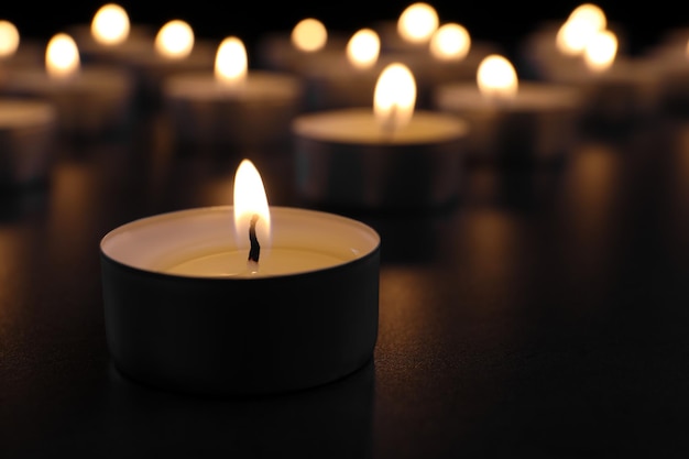 Burning candle on table in darkness closeup with space for text Funeral symbol