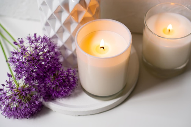burning candle and violet allium flowers on white tray
