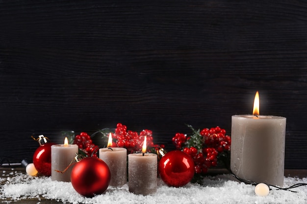 Burning candles and Christmas accessories with snow on wooden background