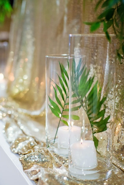 Burning candles in glass vases with palm leaf near wedding table with golden sequin tablecloth