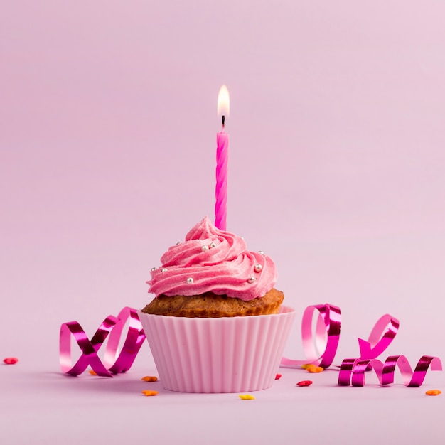 Burning candles over the muffins with sprinkles and streamers on pink backdrop