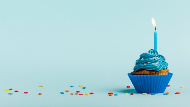 Photo burning candles on muffins with star sprinkles against blue backdrop