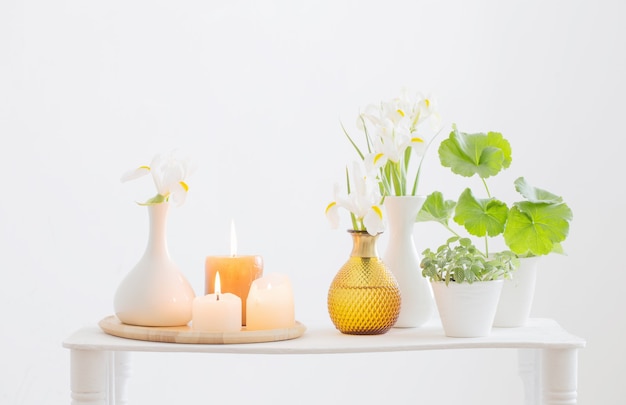 Burning candles and spring flowers on wooden shelf in white interior