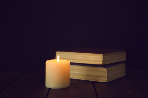 Burning candles and stack of books on wooden table in darkness