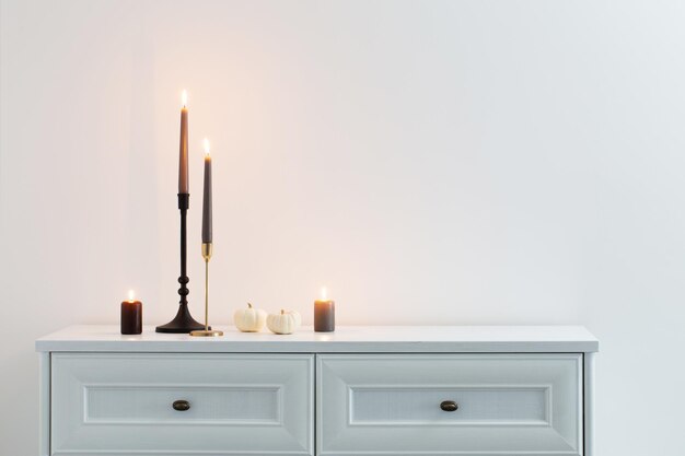 Burning candles on white wooden shelf in white interior