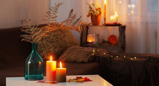 Burning candles with autumn decor on white table at home