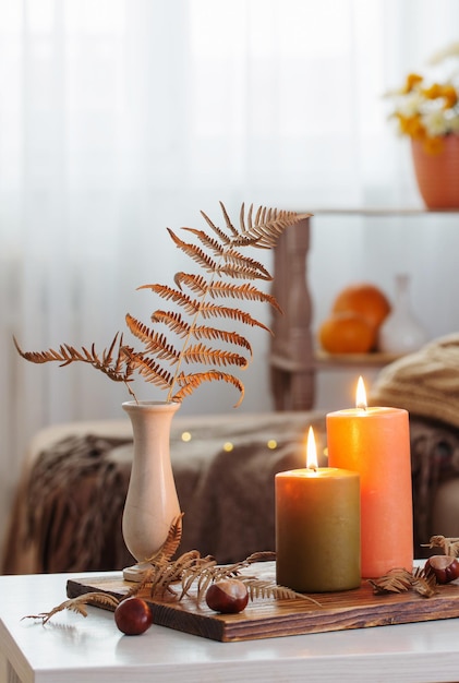 Burning candles with autumn decor on white table at home