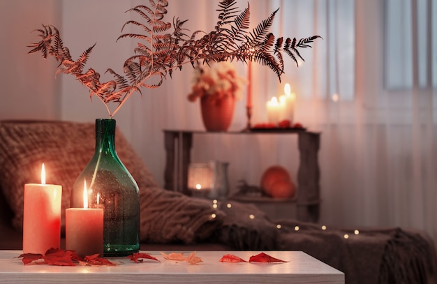 Burning candles with autumn decor on white table at home