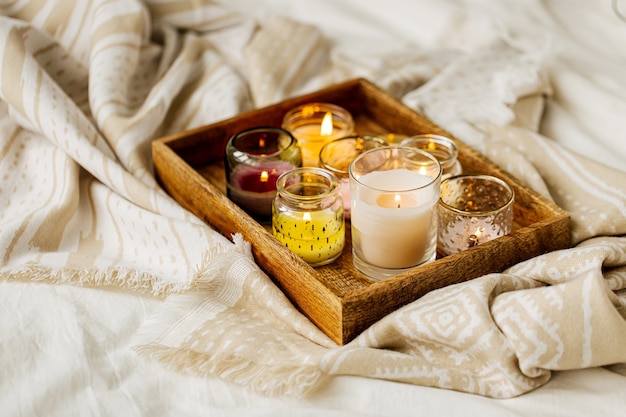 Burning candles on wooden tray with warm plaid in bed.  Scandinavian style. Hygge concept.