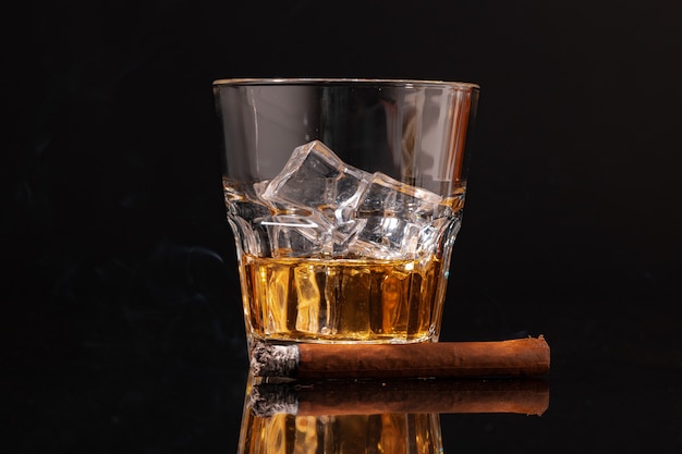 Горящая сигара и стакан виски на черном фоне