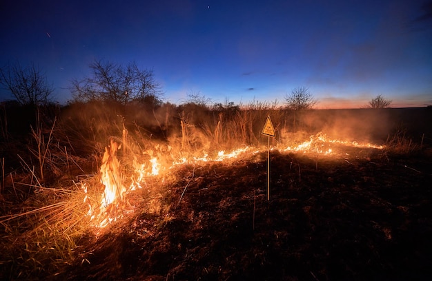 Photo burning dry grass and warning sign in field at night