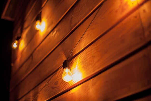 Burning garlands garland on a wooden background. Light bulbs on wooden background. Evening Wooden Stage In The Garden With Lamps For Parties Or Wedding