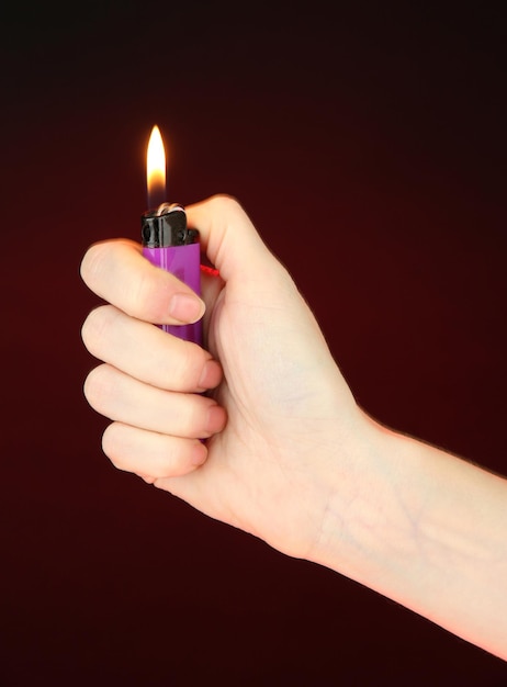 Burning lighter in female hand on dark red background