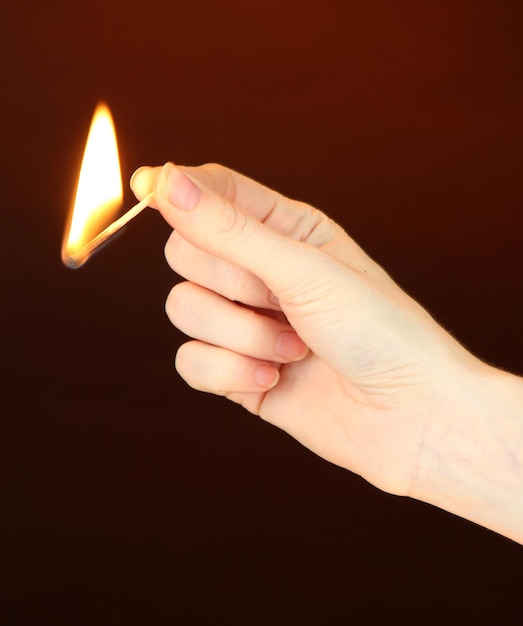 Burning match in female hand on dark brown background