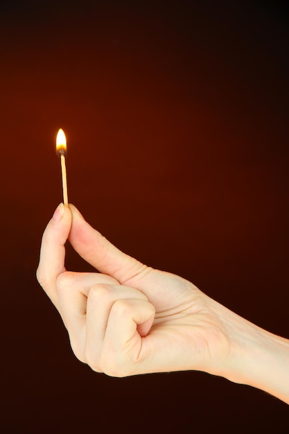 Burning match in female hand on dark brown background