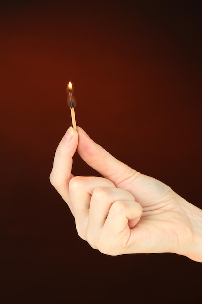 Burning match in female hand on dark brown background