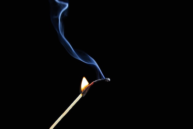 검은 배경에 파란색 연기 기둥이 있는 불타는 성냥 반쪽.