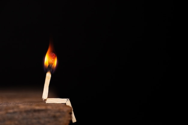 Burning match human sitting on wooden table on a dark background. 