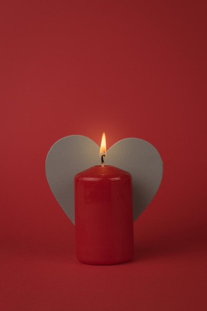 A burning red candle and a gray wooden heart on a red background. The concept of a romantic relationship.