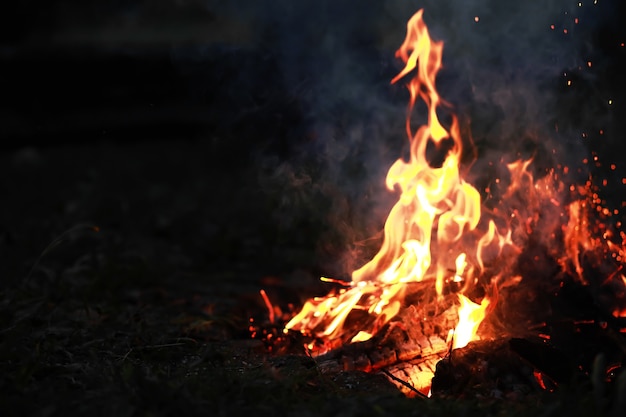 Scintille roventi brucianti volano da un grande fuoco. carboni ardenti, particelle in fiamme che volano via su sfondo nero.