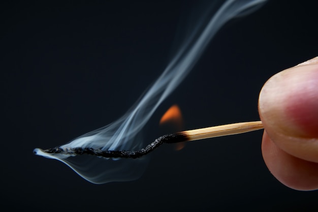 Burning and Smoking wooden match in hand on dark