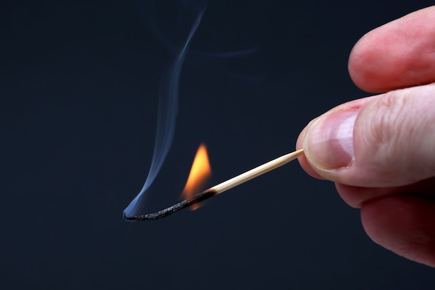 Burning and Smoking wooden match in hand on dark