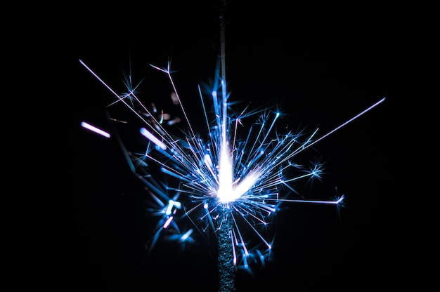 Burning sparkler in blue and white light on a black background Closeup photo of Christmas and new year sparkler Can be used like a wallpaper or postcard