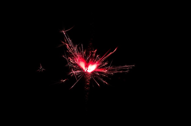 Burning sparkler in red and white light on a black background Closeup photo of Christmas and new year sparkler Can be used like a wallpaper or postcard