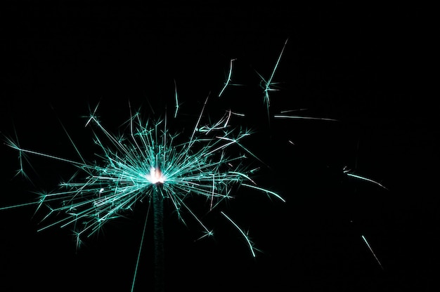 Burning sparkler in turquoise and white light on a black background Closeup photo of Christmas and new year sparkler Can be used like a wallpaper or postcard