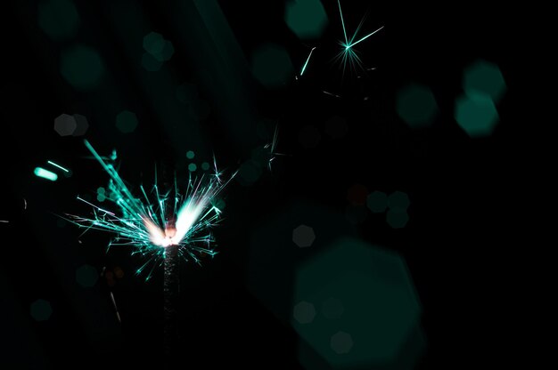 Photo burning sparkler in turquoise and white light on a black background closeup photo of christmas and new year sparkler can be used like a wallpaper or postcard