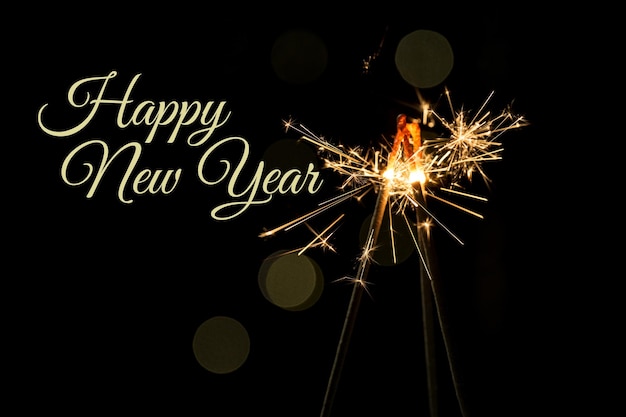 burning sparklers with beautiful sparks on a dark background with happy new year text