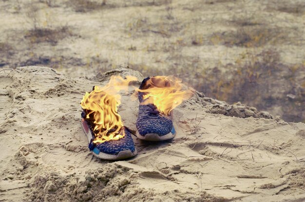 Photo burning sports sneakers or gym shoes on fire stand on sandy beach coast athlete burned out physical exertion during training concept