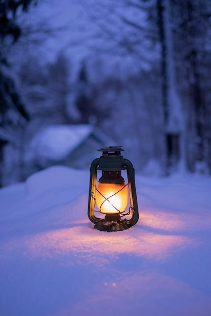 Burning vintage lantern in winter night forest Beautiful winter background against the backdrop of a house in village