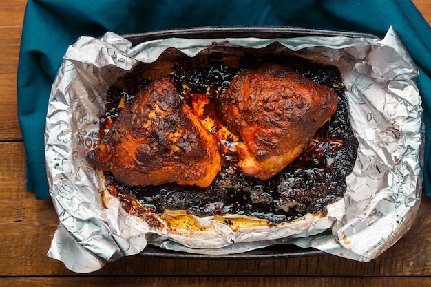 Photo burnt chicken in foil with a golden brown crust on the table in a baking dish